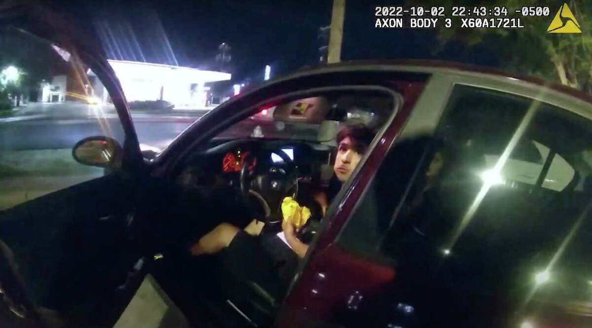 In this image taken Oct. 2, 2022, from a police body camera video and released by the San Antonio Police Department, Erik Cantu looks toward San Antonio police officer James Brennand while holding a hamburger as the officer opens the car door in San Antonio.